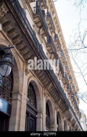 Barcelona, Spanien - 10. März 2026: Flacher Blick auf eine historische Wohnhausfassade in Barcelona mit kunstvollen Steinbögen und Schmiedeeisen Stockfoto