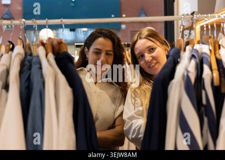 Zwei junge Frauen stöbern in den Kleiderständern und genießen eine Einkaufstherapie während des Einkaufs Stockfoto