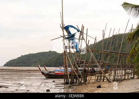 Krabi Thailand 19. Februar 2026. Bambus Angelausrüstung steht an der Küste in der Nähe von geerdeten Booten bei Ebbe in Khlong Muang. Stockfoto