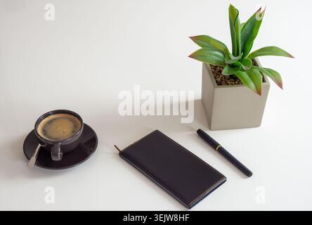 Minimalistischer Schreibtisch mit Kaffee, Stift, Notebook und Pflanze Stockfoto