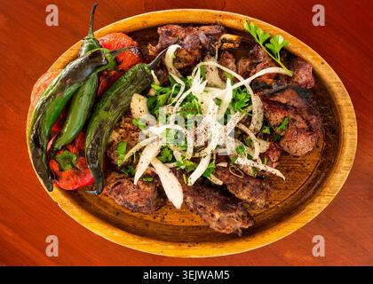 Traditionelle Schaschlik serviert mit gegrillten Paprika, Zwiebeln und frischen Kräutern auf einem Holzteller, Aserbaidschan. Stockfoto