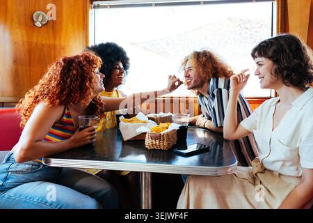 Multiethnische Gruppe junger glücklicher Freunde, die sich im Vintage Diner Burger House Restaurant zusammenschließen - vielfältige Gruppe glücklicher junger Freunde, die Snacks und d Stockfoto