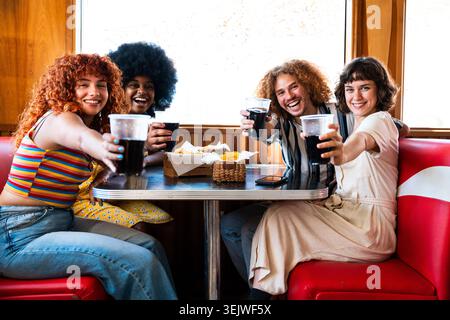 Multiethnische Gruppe junger glücklicher Freunde, die sich im Vintage Diner Burger House Restaurant verbünden - vielfältige Gruppe junger Freunde lachen, trinken i Stockfoto