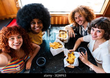 Multiethnische Gruppe junger glücklicher Freunde, die sich im Vintage Diner Burger House Restaurant zusammenschließen - vielfältige Gruppe junger Freunde, die sich treffen, lächeln und engagieren Stockfoto