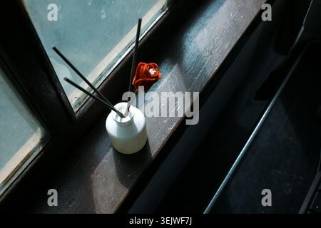 Minimalistischer Reed-Diffusor mit roter Blume auf Vintage-Fensterbank, sanftes Sonnenlicht-Innendesign, gemütliche Atmosphäre und entspannter Lebensstil Stockfoto