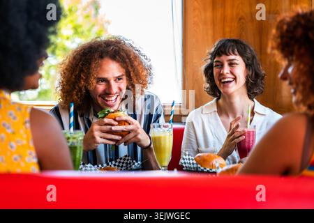 Multiethnische Gruppe junger glücklicher Freunde, die sich im Vintage Diner Burger House Restaurant zusammenschließen - junge glückliche, vielfältige Freunde treffen sich und essen Spaß Stockfoto