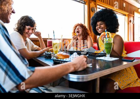 Multiethnische Gruppe junger glücklicher Freunde, die sich im Vintage Diner Burger House Restaurant zusammenschließen - junge glückliche Leute, die Burger und Getränke genießen, Bonding at Stockfoto