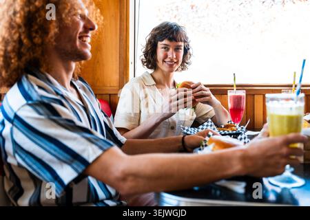 Multiethnische Gruppe junger glücklicher Freunde, die sich im Vintage Diner Burger House Restaurant zusammenschließen - Gruppe glücklicher Freunde, die sich im A VI zusammenschließen und essen Stockfoto
