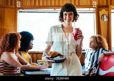 Multiethnische Gruppe junger glücklicher Freunde, die sich im Vintage Diner Burger House Restaurant verbünden - junge Leute genießen Essen und Trinken, verbinden sich im Restaurant Stockfoto