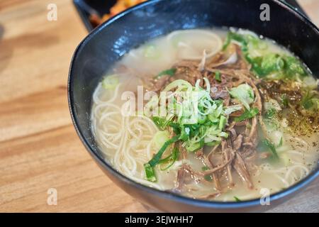 Eine warme Schüssel koreanischer Fleischnudeln besteht aus zartem, geriebenem Fleisch, dünnen Nudeln und frischen Zwiebeln in einer reichhaltigen Brühe, die einen authentischen Alltagsgeschmack vermittelt Stockfoto