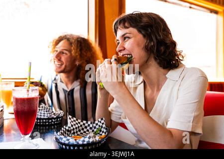 Multiethnische Gruppe junger glücklicher Freunde, die sich im Vintage Diner Burger House Restaurant zusammenschließen - Gruppe von multiethnischen jungen Freunden, die Fast Food und genießen Stockfoto