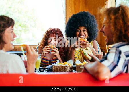 Multiethnische Gruppe junger glücklicher Freunde, die sich im Vintage-Diner-Burger-House-Restaurant verbünden - junge, abwechslungsreiche Freunde, die Fast Food genießen, lächeln und lachen Stockfoto