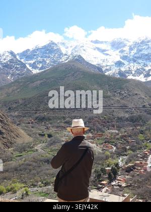 Ein englischer Tourist mit seinem panamahut bewundert die majestätische Landschaft der schneebedeckten Gipfel des Atlasgebirges. Stockfoto