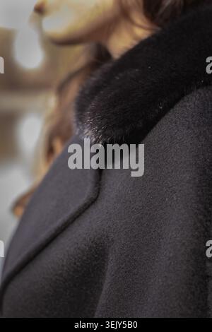 Das Bild zeigt eine detaillierte Nahaufnahme eines hochwertigen Wintermantels aus schwarzer Wolle mit luxuriösem, glänzendem Pelzkragen, der von einer Frau getragen wird. Stockfoto