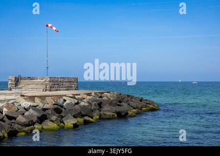 Küstenmole mit Windsocken über der felsigen Küste und ruhigem Meer unter klarem blauen Himmel Stockfoto