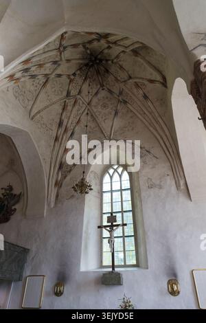 Innenansicht der mittelalterlichen Kirche mit gewölbter Decke, einem hohen Bogenfenster und einem darunter liegenden Kruzifix. Stockfoto