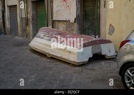 Ein verwittertes Boot sitzt verkehrt auf einer schmalen, gepflasterten Straße. Es wurde wahrscheinlich zur Wartung oder Winterlagerung an Land gebracht, in dieser ruhigen Stadt. Stockfoto