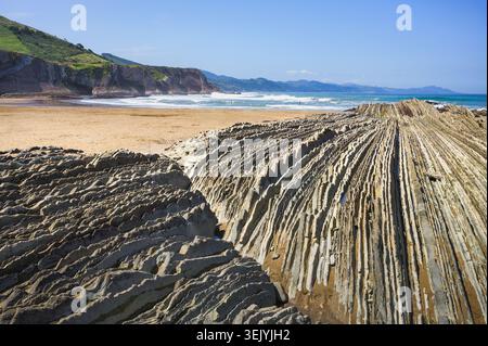Dramatische Faltfelsen am wilden Atlantischen Sandstrand mit türkisfarbenen Wellen und grünen Klippen, Baskenland, Spanien Stockfoto