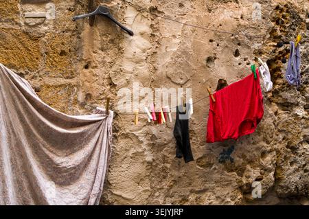 Die Einwohner hängen ihre frisch gewaschene Wäsche, einschließlich eines roten Hemdes und Socken, an einen Leinen an eine alte, strukturierte Steinmauer, um darunter zu trocknen Stockfoto