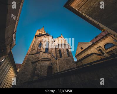 Niedrigwinkelaufnahme einer majestätischen mittelalterlichen Steinkirche vor einem klaren blauen Himmel. Gotische Fenster und altes Mauerwerk einer historischen Kathedrale in Prag. Stockfoto