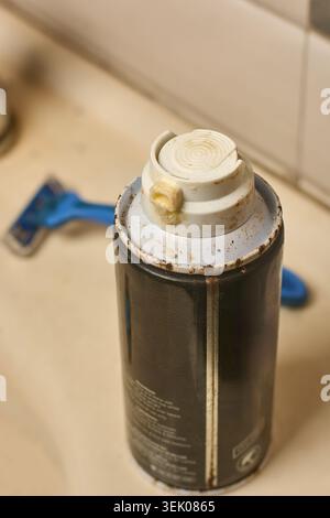 Alte, rostige, metallische Rasierschaum-Dose auf der Oberfläche des Badezimmerwaschbeckens, gebrauchter Behälter mit getrockneten gelben Rückständen um die Düse, Draufsicht Soft Focus Stockfoto