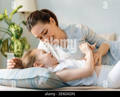 Herzzerreißender Moment zwischen einer liebevollen Mutter und ihrer lachenden Tochter, die in einem hellen, gemütlichen Wohnzimmer schöne Zeit und spielerische Zuneigung genießen. Dies Stockfoto