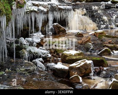 Blick auf schwere Eiszapfen, die an felsigen Ufern über einem gefrorenen Fluss hängen Stockfoto