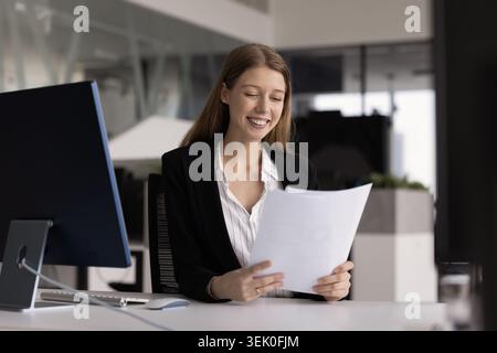 Geschäftsfrau, die gedruckte Dokumente hält und lächelt, während sie gute Nachrichten liest Stockfoto