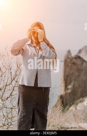 Kopfschmerzen Migräne Schmerzen junge Frau, die auf einer Klippe am Meer steht und unter Stress bei Sonnenuntergang leidet Stockfoto