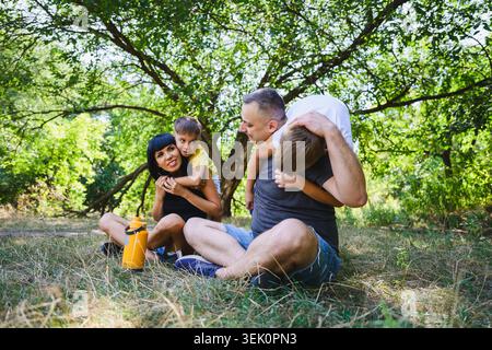 Eltern und zwei Söhne genießen spielerische Momente zusammen in einem grünen Park. Familie im Freien mit Lachen, Zuneigung und guter Zeit in der Natur. Stockfoto
