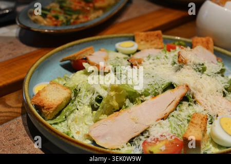 Nahaufnahme eines Caesar-Salats mit gegrillten Hähnchenscheiben, Croutons, halbierten gekochten Eiern und Kirschtomaten auf einem rustikalen Steinteller. Stockfoto