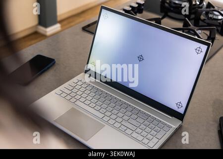 Silberner Laptop, der offen auf der Küchenarbeitsplatte sitzt und Fadenkreuze zeigt, Smartphone, Gasherd in der Nähe Stockfoto