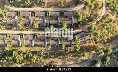 Aus der Vogelperspektive zeigt Reihen verlassener Hotelbungalows oder ländlicher Häuser in einem vernachlässigten Anwesen, umgeben von trockener Vegetation und gewundenen Straßen, reflektierend Stockfoto
