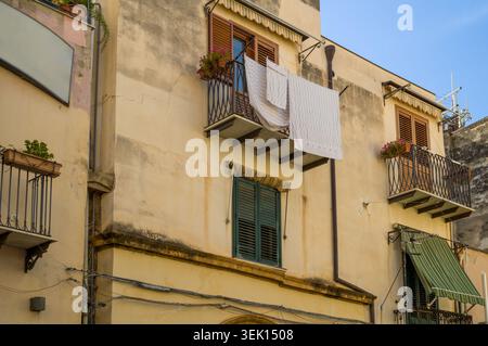 Ein Einheimischer hängt frische weiße Bettwäsche auf seinem Balkon, um in der mediterranen Sonne zu trocknen, eine klassische und effiziente tägliche Arbeit in diesem traditionellen, s Stockfoto