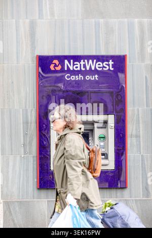 Frau, die an einem NatWest-Geldautomat vorbeiläuft und einen Geldautomaten in einer Bankfiliale in Großbritannien mit Branding versehen hat Stockfoto
