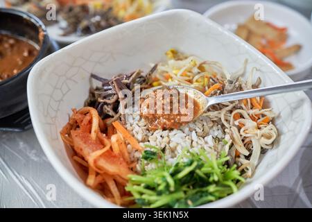 Koreanische Doenjang Bori Bibimbap-Sequenz. Dickflüssige Sojabohnenpaste gemischt mit plumpem Gerstenreis und frischem Gemüse für eine gesunde, rustikale lokale Mahlzeit. Stockfoto