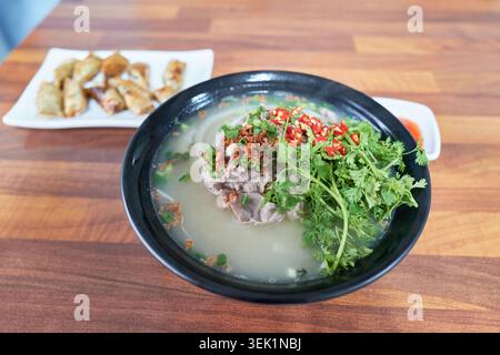 Vietnamesisches Rindfleisch Pho in einer schwarzen Schüssel mit frischem Koriander, Rindfleisch und roten Chilis auf einem Holztisch. Ein perfekter Schuss authentischer asiatischer Speisen. Stockfoto