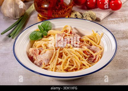 Appetitliche Spaghetti Carbonara in weißer Schüssel mit Basilikumgarnitur. Cremige Sauce, knuspriger Speck, goldene Nudeln. Warmes Licht sorgt für satte Texturen Stockfoto