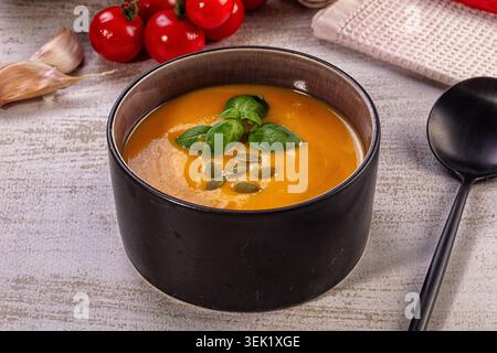 Kräftige, orange Kürbissuppe in dunkler Keramikschale. Garniert mit frischen Basilikumblättern und gerösteten Kürbiskernen. Warmes, einladendes Herbstessen, gesundes Essen Stockfoto