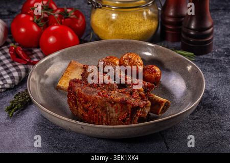 Appetitliche gegrillte Rinderrippchen glasiert mit Senfsauce serviert mit gebratenen Kartoffeln in einer rustikalen grauen Schüssel. Herzhaftes Gourmet-Essen auf dunklem Backgrou Stockfoto