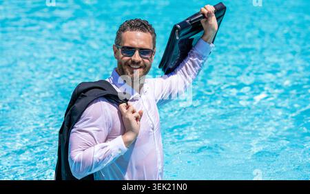 Geschäftserfolg. Geschäftsmann in Anzug im Swimmingpool. Aufgeregter Geschäftsmann im Nassanzug im Schwimmbad. Remote-Arbeiten. Business Drink Sommercocktail Stockfoto