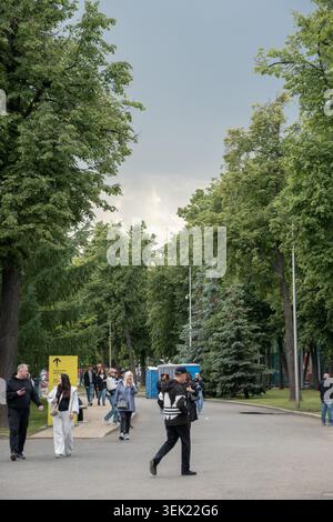 Moskau, Russland - 30. Mai 2026: Besucher spazieren entlang der von Bäumen gesäumten Allee im Luschniki-Park unter dunklen Sturmwolken nach Regen, umgeben von dichten Gewitterwolken Stockfoto