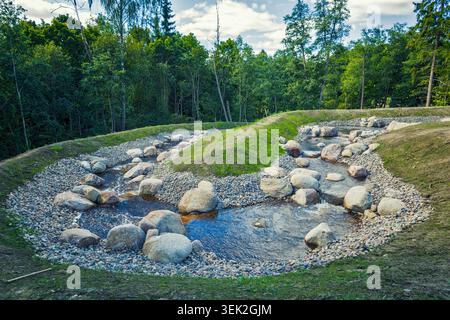 Espoo, Finnland - 01.08.2020: Kleiner Wasserlauf gesäumt von glatten Steinen und Kieselsteinen, der sich durch einen grünen Sommerwald schlängelt Stockfoto