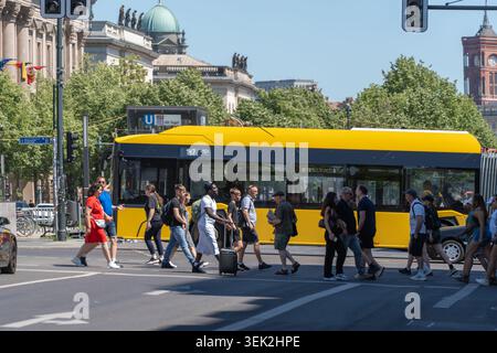 Deutschland, Berlin, 25. Mai 2026. Ein gelber Berliner Bus fährt an Menschenmassen unter den Linden in der Nähe historischer Kuppeln und Türme vorbei. Die sonnige Straßenszene zeigt Pede Stockfoto