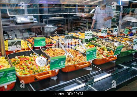 Verschiedene frisch zubereitete georgianische Speisen, Reis und Gemüse in Keramiktabletts mit Preisschildern in georgischer und englischer Sprache unter einer Glasvitrine. Stockfoto