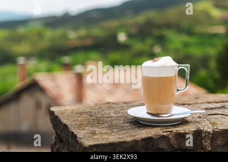Tasse aufgeschäumter Latte Kaffee auf der Steinterrasse mit malerischem Blick auf die Landschaft Stockfoto
