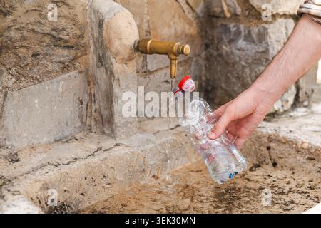 Wiederverwendbare Wasserflasche aus dem öffentlichen Trinkbrunnen im Bergdorf nachfüllen Stockfoto