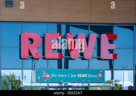 Deutschland, Berlin, 25. Mai 2026. Ein großes rotes REWE-Schild erhebt sich über einem türkisfarbenen Jubiläumsbanner. Die Fassade kombiniert Supermarkt-Branding und Glas Stockfoto