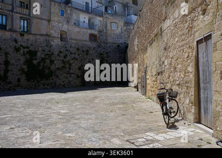 Ein Fahrrad mit einem Schub, das sich gegen eine gelbe Ziegelmauer neben einer alten Tür im historischen Teil von Otranto Apulien in süditalien lehnt Stockfoto