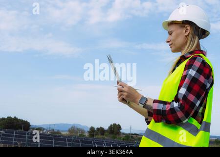 Ingenieurin trägt Schutzhelm und Sicherheitsweste, arbeitet mit einem digitalen Tablet an einer Solaranlage und überwacht nachhaltige Energieerzeugung Stockfoto